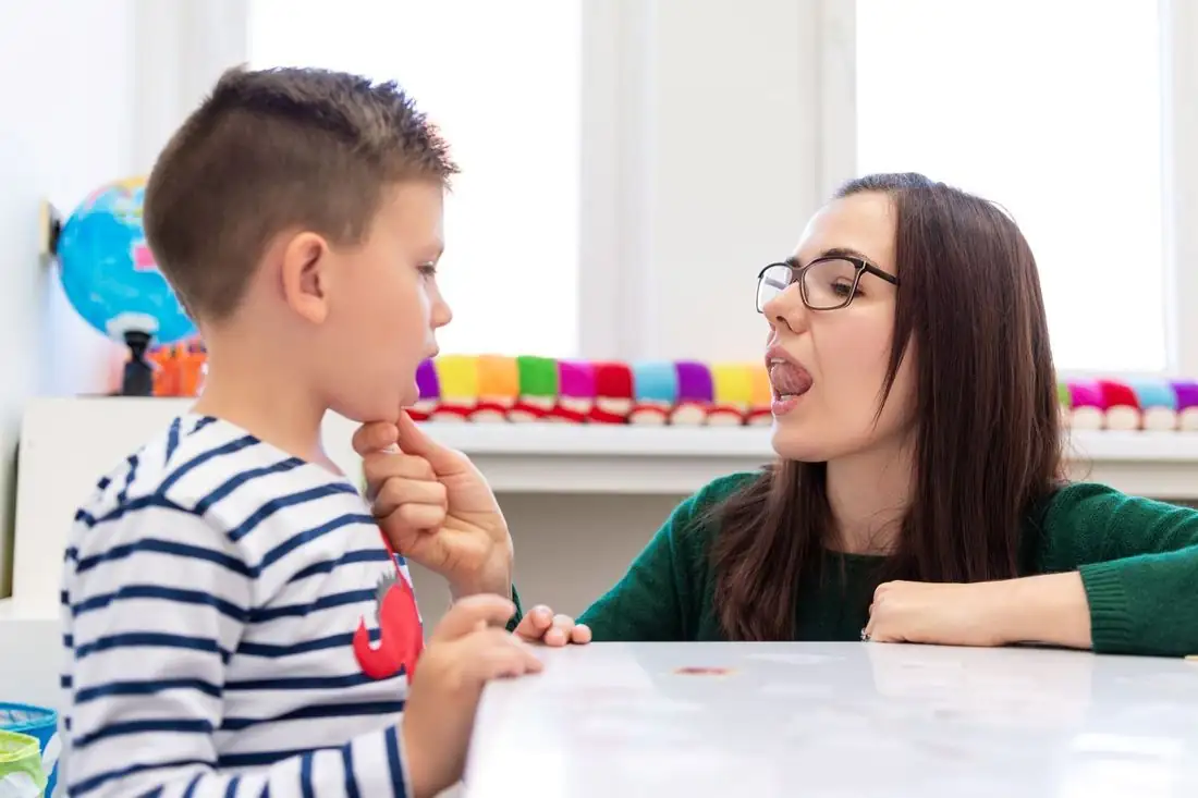 A speech-language pathologist practising sounds with a young boy at a table